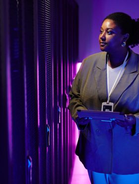 Portrait of female system administrator inspecting data network in server room lit by neon light, copy space