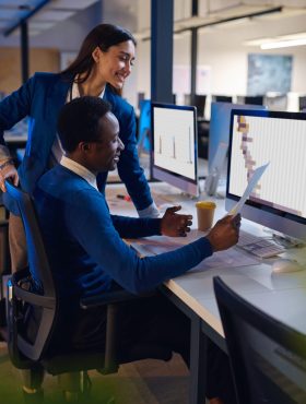 Two happy managers working in night office. Male and female workers, dark business center interior on background, modern workplace