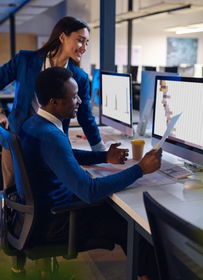 Two happy managers working in night office. Male and female workers, dark business center interior on background, modern workplace